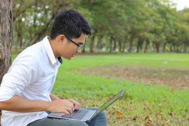 Doğa park açık kopya alan arka plan ile bir dizüstü bilgisayarda yazarak Asya yakışıklı genç.