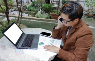 Yakışıklı genç işadamı geniş açı çekim telefonda laptop ve evrak ile yaptığı çalışmalarla halka açık konuşuyor.