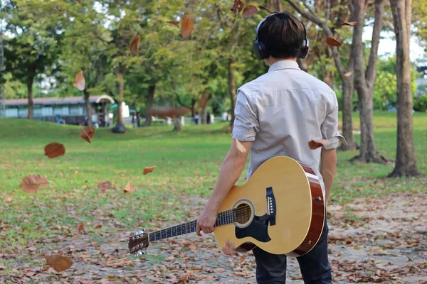 헤드폰으로 남자의 어쿠스틱 기타를 들고와 공원에서 나뭇잎 떨어지고 — 스톡 사진