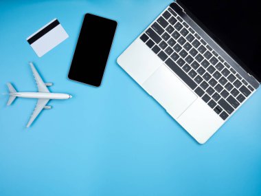 Kopya alanı ile izole mavi arka plan üzerinde laptop, smartphone, kredi kartı ve uçak üstten görünüm.