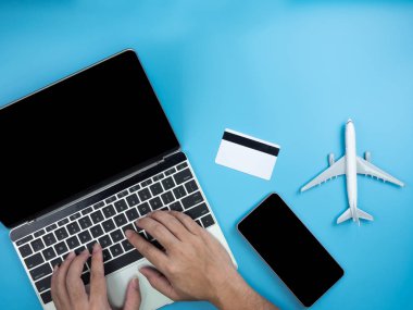 Dizüstü bilgisayar, akıllı telefon, kredi kartı ve kopya alanı izole mavi artalanla uçağa el üstten görünüm.
