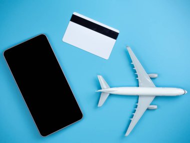 Kopya alanı izole mavi zemin üzerine smartphone, kredi kartı ve uçak üstten görünüm.