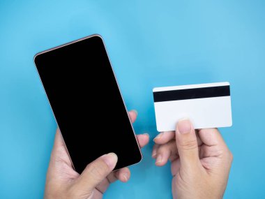 Mobil akıllı telefon ve kredi kartı holding eller izole arka plan mavi. Internet ve alışveriş online kavramı.
