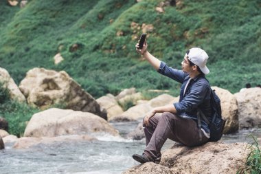Fotoğraf veya selfie açık havada doğal doğa arka plan alarak genç Asian traveler adam. Yaşam tarzı ve gevşeme kavramı.