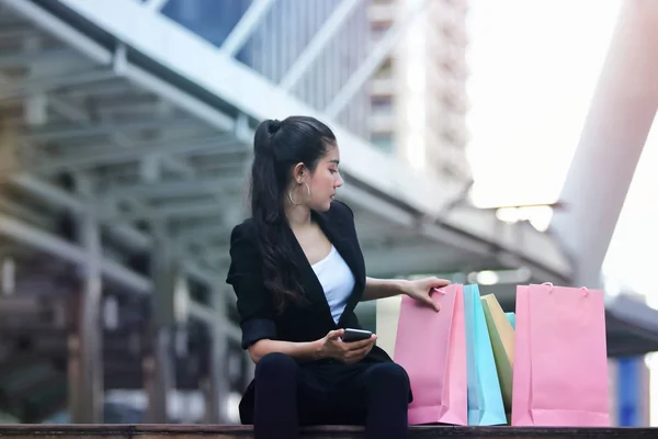 Vrolijke Jonge Aziatische Vrouw Met Kleurrijke Boodschappentas Zitten Open Lucht — Stockfoto