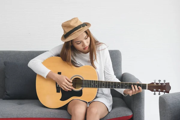 Rilassato giovane donna asiatica suonare la chitarra acustica in soggiorno . — Foto Stock