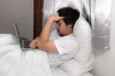 Sinirli yatak odasında yatakta dizüstü bilgisayar ile Asyalı adam vurguladı.
