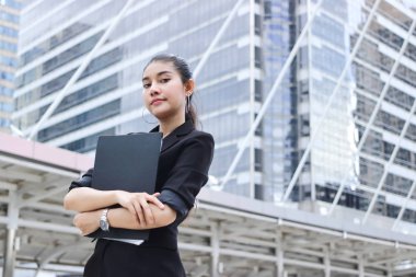 Ofisin önünde duran evrak klasörüyle kendinden emin genç Asyalı iş kadını..