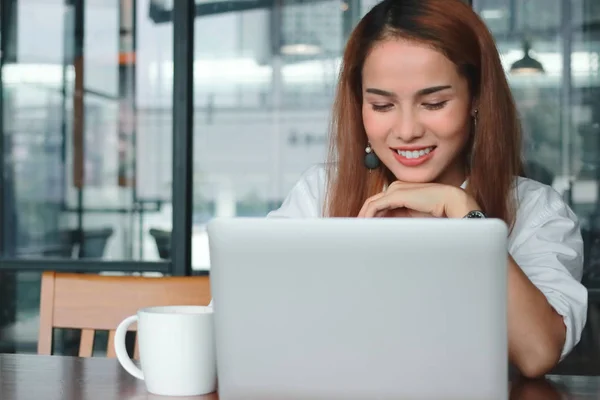 Улыбающаяся молодая азиатская деловая женщина с ноутбуком работает в современном офисе. — стоковое фото