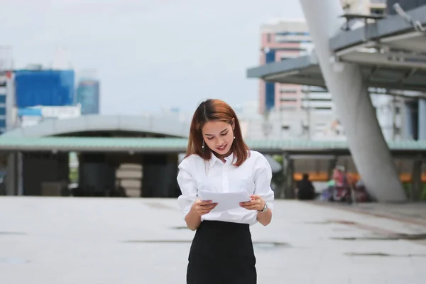 Улыбающаяся молодая азиатская деловая женщина анализирует диаграммы или бумажную работу во время ходьбы — стоковое фото