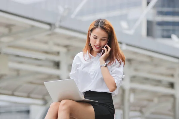 Привлекательная молодая азиатская деловая женщина, использующая ноутбук и мобильный смартфон для работы вне офиса. — стоковое фото