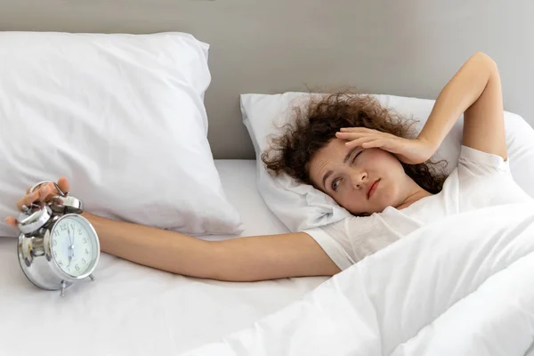 Young lazy woman putting her alarm clock off on the bed in bedroom — Stock Photo, Image