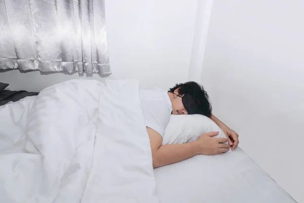 Young Asian man with blindfold eye mask sleeping on the white bed in bedroom.