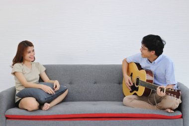 Oturma odasında birlikte akustik gitar çalan rahat bir Asyalı çift. Aşk ve romantizm kavramı.