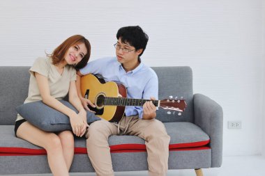 Çekici genç Asyalı çift oturma odasında birlikte akustik gitar çalıyor. Aşk ve romantizm kavramı.