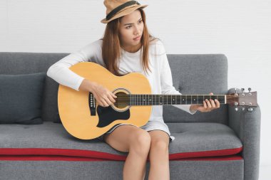 Oturma odasında akustik gitar çalan rahat bir Asyalı kadın..