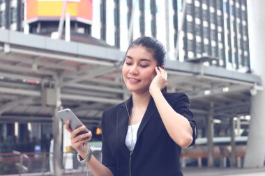 Rahat genç Asyalı kadın şehir merkezinde cep telefonuyla müzik dinliyor..