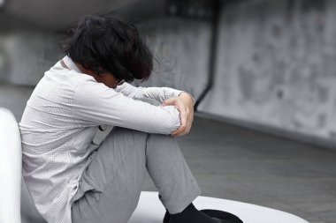 Depresyondaki Asyalı genç iş adamı üzgün ve ofisin dışında oturuyor. İşsizlik ve işten çıkarma kavramı.