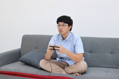 Genç Asyalı adam oturma odasında joystick ile oyun oynuyor..