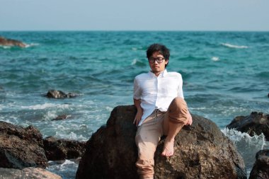 Hafta sonu tatillerinde deniz kenarında oturan rahat, yakışıklı Asyalı genç adam..