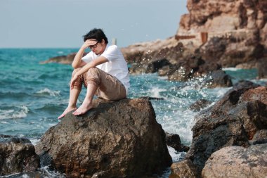 Depresyondaki Asyalı genç adam deniz kenarında oturuyor ve hayal kırıklığı yaşıyor..