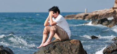 Depresyondaki genç Ais 'in panoramik görüntüsü. Deniz kenarında oturan ve hayal kırıklığı hisseden genç bir adam..