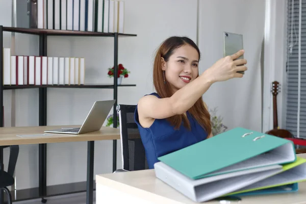 Relaxed young Asian business woman taking a picture or selfie in office