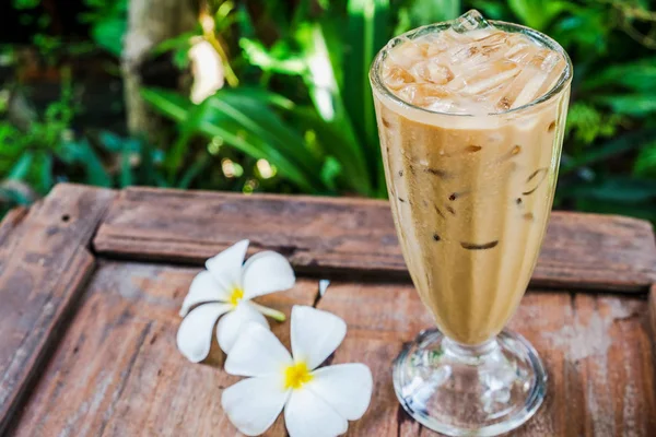 Ahşap zemin üzerinde beyaz plumeria çiçekli bahçesinde kahve cam.