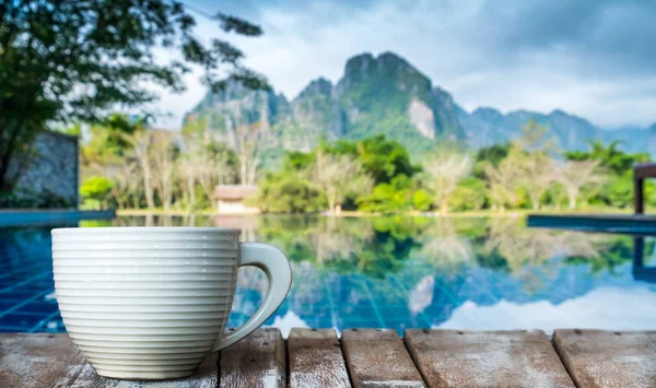 Una taza de café blanco en la mesa de madera junto a la piscina — Foto de Stock