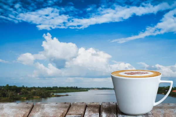 Nehrin kenarındaki ahşap masada beyaz bir fincan kahve. — Stok fotoğraf