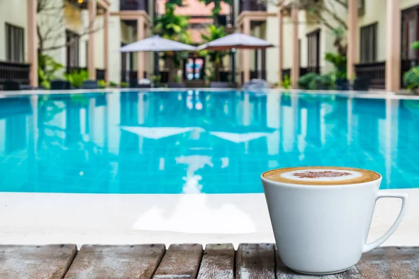 Egy csésze fehér kávé a fa asztalon a medence mellett.. Stock Kép