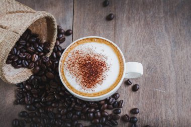 Kahve çekirdekleri çuvalda, kahve fincanı da tahta masanın arkasında.