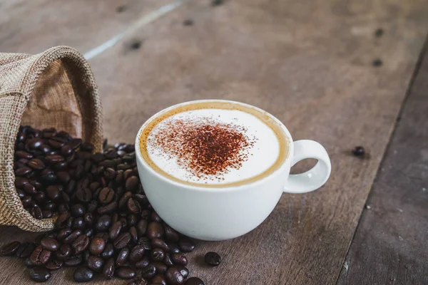Biji kopi dalam karung dengan cangkir kopi di atas meja kayu backg — Stok Foto