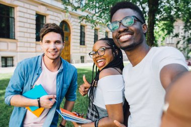 Eğitim, yaşam tarzı, eğlence ve teknoloji kavramı. Farklı ülkelerden ve yarışlardan neşeli arkadaşlar arka aydınlatma ile selfie çekiyor. Birlikte eğlenen gençlerle mutlu gençlik konsepti.