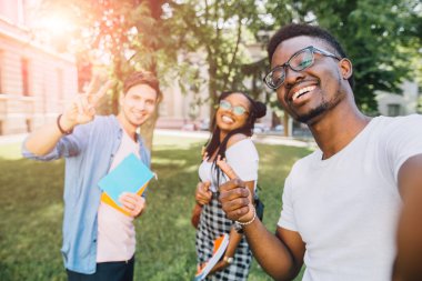 Eğitim, eğlence ve teknoloji kavramı. Farklı ülkelerden ve yarışlardan neşeli arkadaşlar arka aydınlatma ile selfie çekiyor. Üniversite kampüsünde eğlenen mutlu gençler. Güneş parlama etkisi.