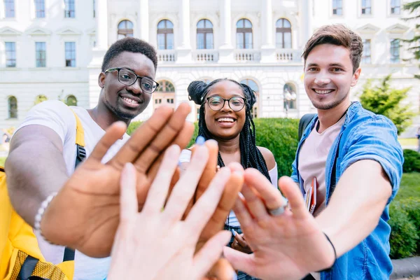 Trois étudiants multiethniques vous saluent, vous tenant les paumes ouvertes, en plein air au-dessus du bâtiment universitaire. Groupe diversifié Personnes High Five Concept . — Photo