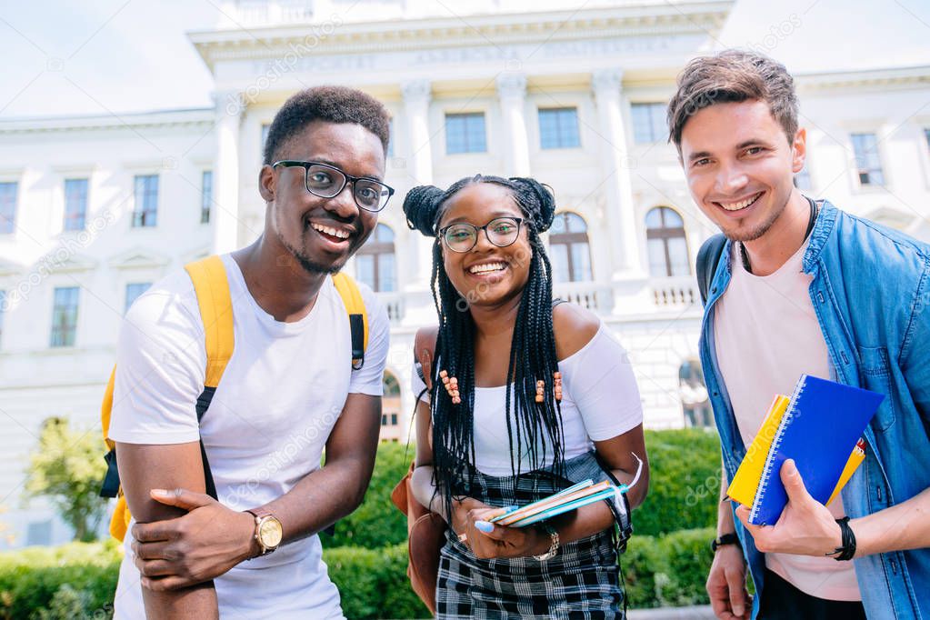 Low angle view of three positive defferent races friends students on university campus in autumn time.