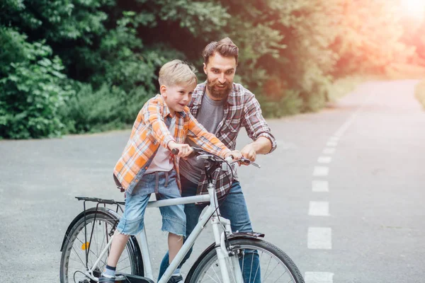 Счастливый отец учит своего сына кататься на велосипеде на открытом воздухе в летнем парке. Эффект гларте Солнца . — стоковое фото