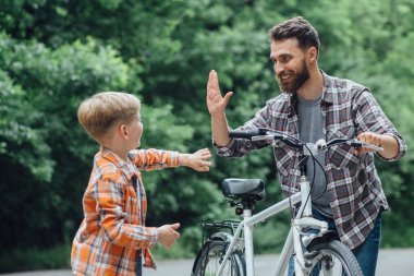 Baba eski bisikletini oğlu için verir. Parkta bisiklet sürerken yüksek beş veren mutlu çocuk çocuk.
