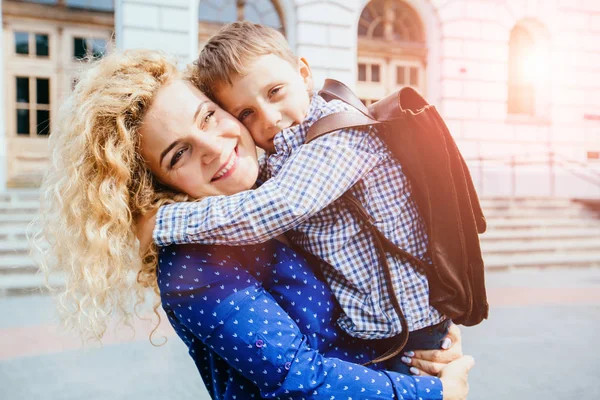 Vergadering na school. Gelukkig blond krullend Kaukasische moeder en zoon lopen, knuffelen, wervelende om elkaar te ontmoeten in de voorkant van het schoolgebouw buiten. — Stockfoto