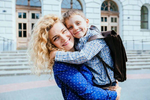 Vergadering na school. Gelukkig blond krullend Kaukasische moeder en zoon lopen, knuffelen, wervelende om elkaar te ontmoeten in de voorkant van het schoolgebouw buiten. — Stockfoto