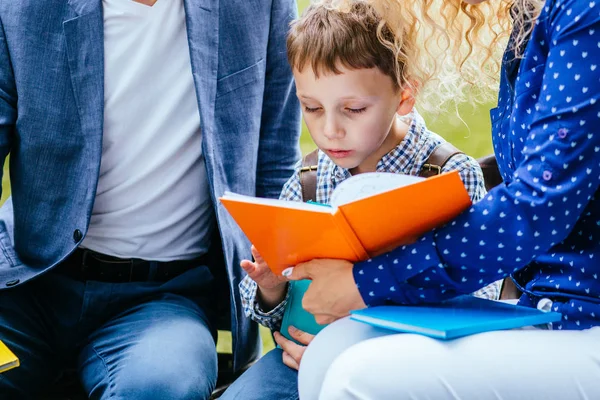 Betrokken kind jongen zittend tussen moeder en vader en het lezen van interessante boek buiten. — Stockfoto