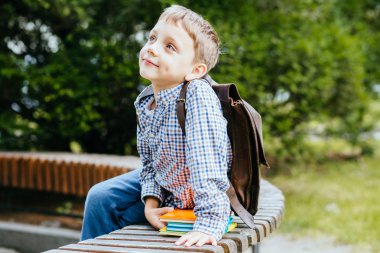 Eğitim ve insan kavramı-sırt çantası ve parlak renkli kitaplar ile utangaç öğrenci çocuk yeşil arka plan açık portre üzerinde koltuk oturuyor.