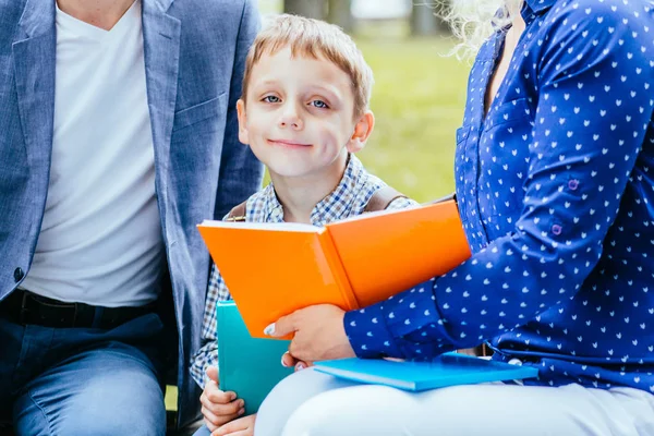 Помолвленный мальчик сидит между матерью и отцом и читает интересную книгу на открытом воздухе . — стоковое фото