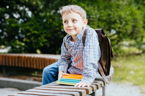 Onderwijs en mensen concept-verlegen student jongen met rugzak en heldere kleurrijke boeken zittend op Bank over groene achtergrond buiten portret. — Stockfoto