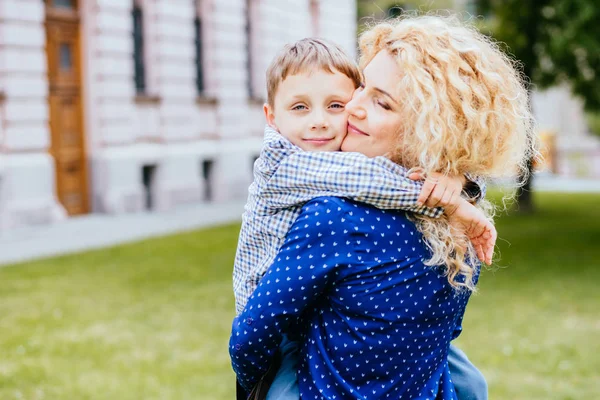 Gelukkig blond krullend moeder plezier met haar kind in zomerpark buiten. Preteen zoon knuffelen zijn mum outdoor. Concept van het moederschap, liefde en Tender momenten . — Stockfoto