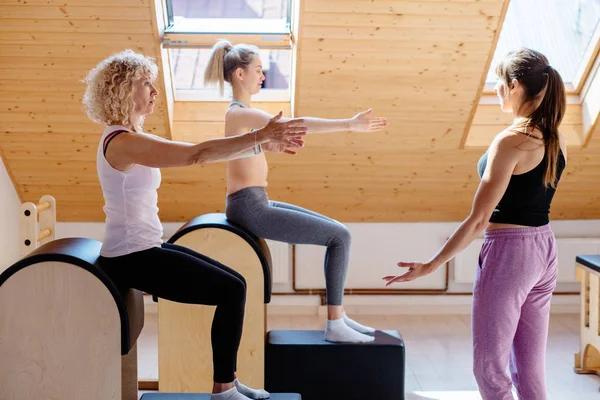 Different generation female is concentrated on exercising on pilates barrels with woman instructor at gym. Sports equipment. Healthy lifestyle rehabilitation concept.