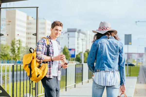 Una joven pareja esperando un autobús en la parada de autobús. Tiempo soleado en el día de verano. Árboles verdes frescos en el distrito de negocios de la capital — Foto de Stock