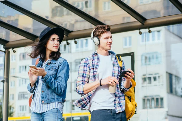 Pareja sonriente mirando hacia otro lado mientras espera en la parada de tranvía en una ciudad . — Foto de Stock