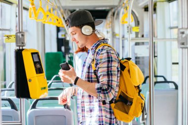 Genç aman kafasında kulaklık ile bir otobüste duruyor ve müzik dinliyor.